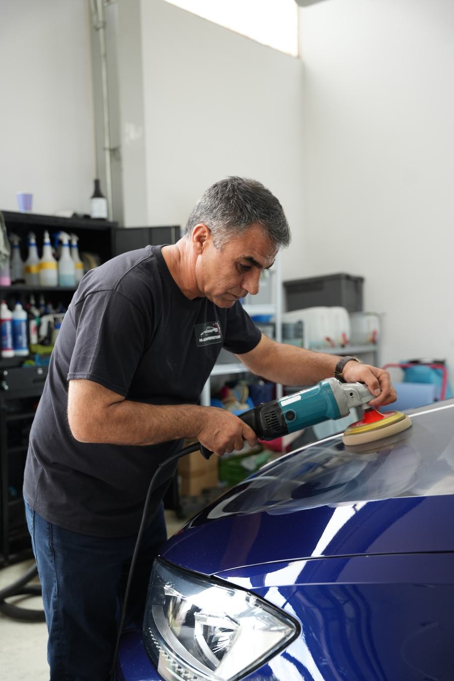 Lackpolitur mit der Poliermaschine an der Motorhaube eines dunkelblauen Fahrzeugs in der Werkstatt